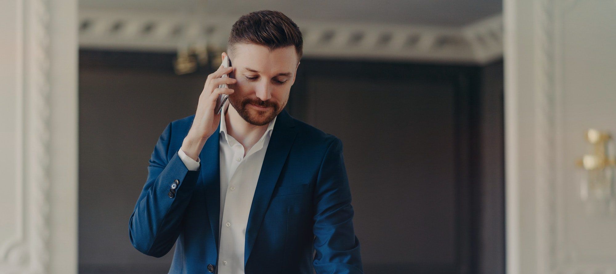 Serious businessman talking on phone while sitting on office desk in modern office